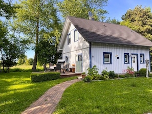 A white house with a tiled roof, a brick pathway leading to the entrance, and a small porch with outdoor furniture.