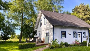A white house with a tiled roof, a brick pathway leading to the entrance, and a small porch with outdoor furniture. - Haus Sternschnuppe - comfortable house with fireplace, sauna, garden, terrace - (Wiek)