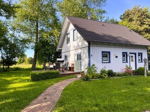 A white house with a tiled roof, a brick pathway leading to the entrance, and a small porch with outdoor furniture.