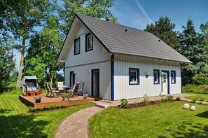 A two-story house with a sloped roof, a deck with outdoor furniture, and a well-maintained lawn. - Haus Sternschnuppe—a cozy house with a fireplace, sauna, garden, and patio— (Wiek)