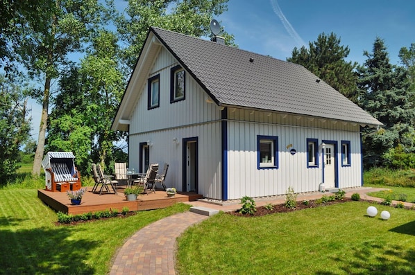A two-story house with a sloped roof, a deck with outdoor furniture, and a well-maintained lawn.