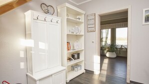 A spacious room with a white wardrobe, open shelving with books and decorative items, a view through an open doorway to a balcony with plants, and a sign on the wall. - Haus Sternschnuppe - comfortable house with fireplace, sauna, garden, terrace - (Wiek)