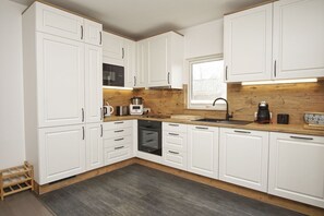 Una cocina moderna con armarios blancos, encimera de madera, horno empotrado y ventana con vistas al exterior.