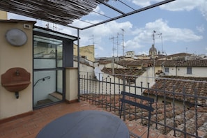 Un balcon donnant sur des bùtiments aux toits de tuiles, avec une rambarde en métal et une petite table.