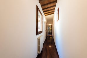 A narrow hallway with wooden flooring, white walls, and a ceiling with exposed beams.