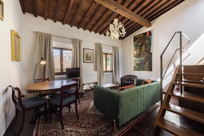 A living room with a wooden ceiling, a green sofa, a dining table with chairs, a television, and a large painting on the wall. - San Giovanni House in Florence by Mmega (Firenze)
