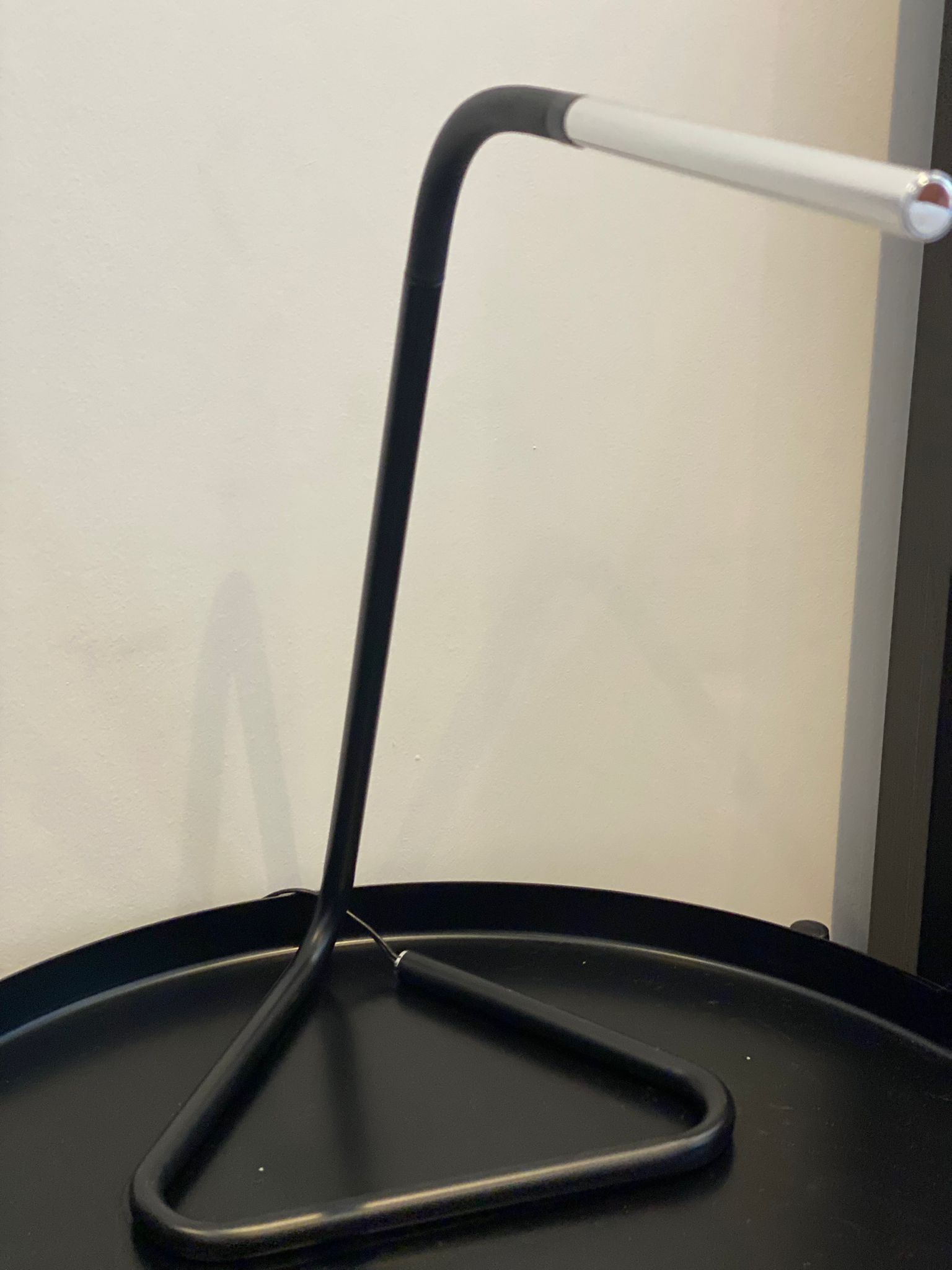 A black metal stand with a white handle against a plain wall.