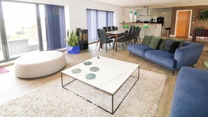 Ein modernes Wohnzimmer mit einer Couch, einem runden Hocker, einem Couchtisch und einem Essbereich mit Stühlen und einem Tisch.
