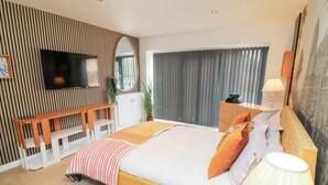Ein modernes Schlafzimmer mit Bett, Nachttisch, Lampe und einem an der Wand befestigten Fernseher.