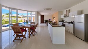 A modern kitchen with a central island, large windows, and a view of a swimming pool. - Villa Lipa Talay Sawng (Koh Samui)