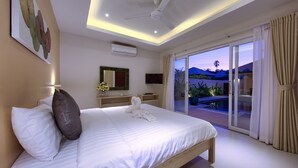 A modern hotel room with a large bed, a ceiling fan, an air conditioning unit, a TV, a small table with a vase of flowers, and a sliding glass door leading to a balcony with a view of the hills. - Villa Lipa Talay Sawng (Koh Samui)