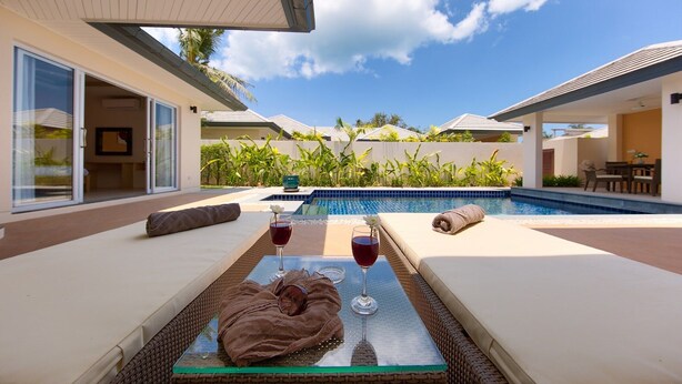 A poolside area with lounge chairs, a glass table with drinks, and a view of a pool and greenery. - Villa Lipa Talay Sawng (Koh Samui)