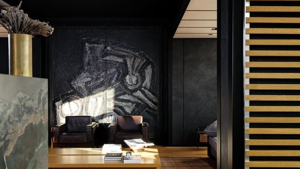 Un intérieur moderne avec un mur foncé, deux fauteuils en cuir, une table basse en bois et un vase décoratif.