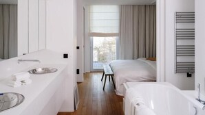 Une chambre d’hôtel moderne dotée d’un grand miroir, d’une baignoire, d’un lit double et d’une fenêtre avec des rideaux.