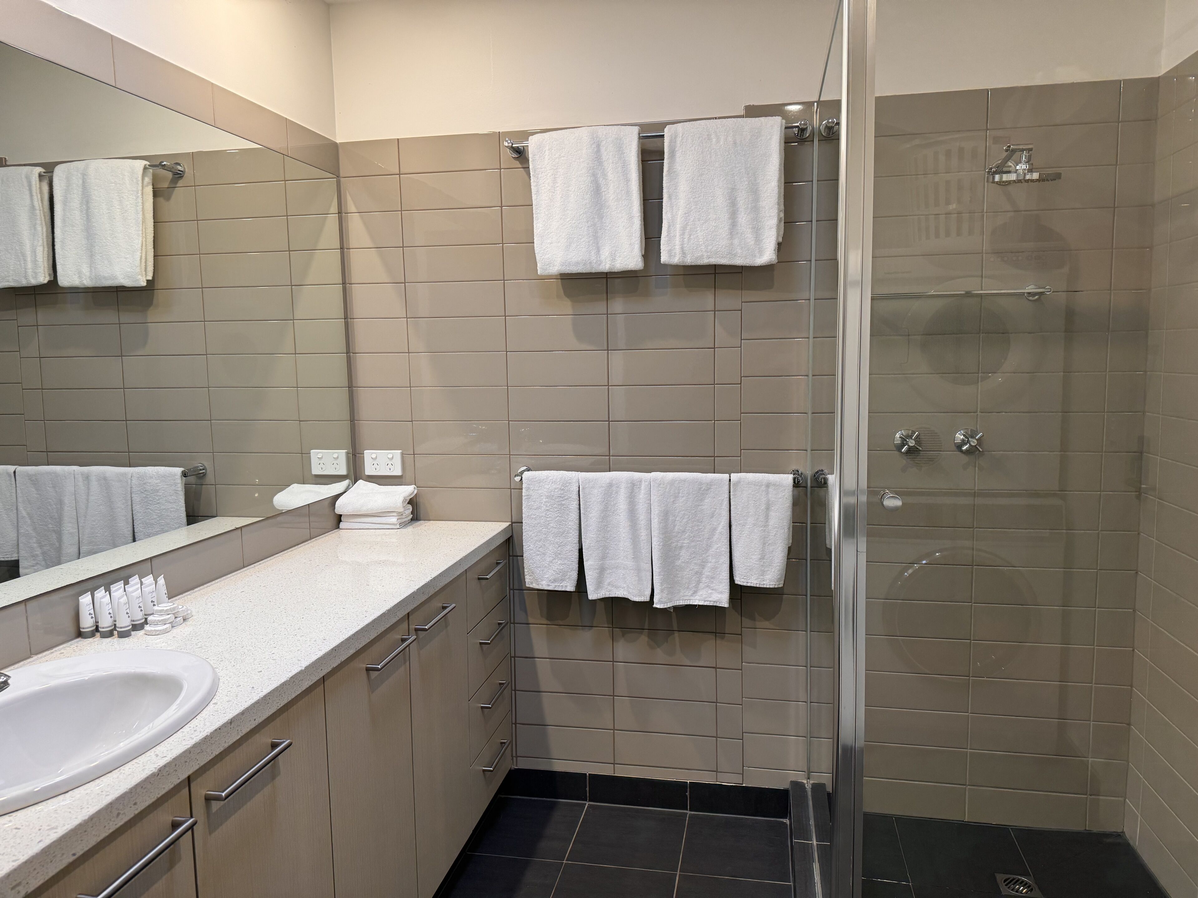 Un baño moderno con lavamanos, espejo y dos toalleros.