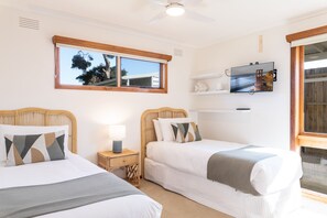 Una habitación con dos camas, ventilador de techo, televisión montada en la pared y ventana con vista a árboles.