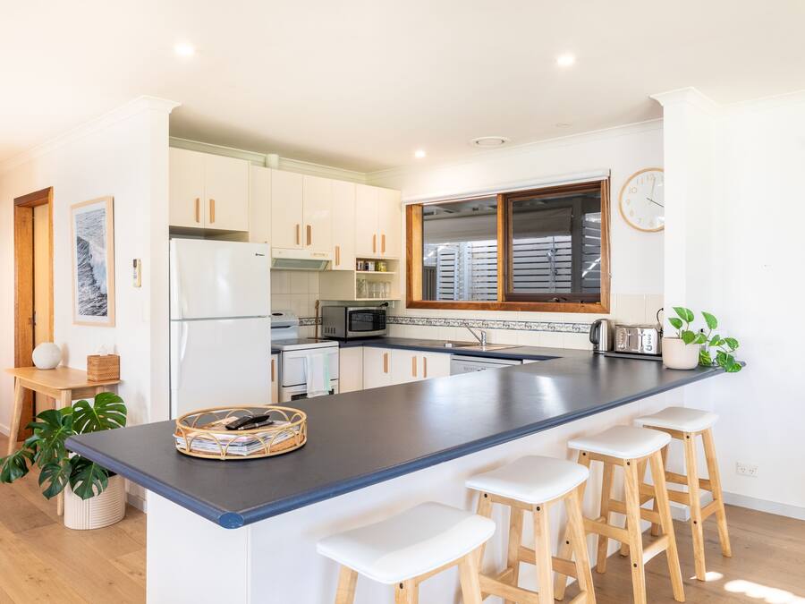 Una cocina moderna con armarios blancos, una isla central con taburetes, un microondas y un reloj en la pared.