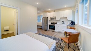 A compact hotel room with a bed, a small table with chairs, a kitchenette, and a window.