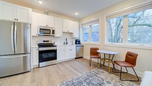 A modern kitchen with white cabinets, stainless steel appliances, and a large window providing a view of trees.