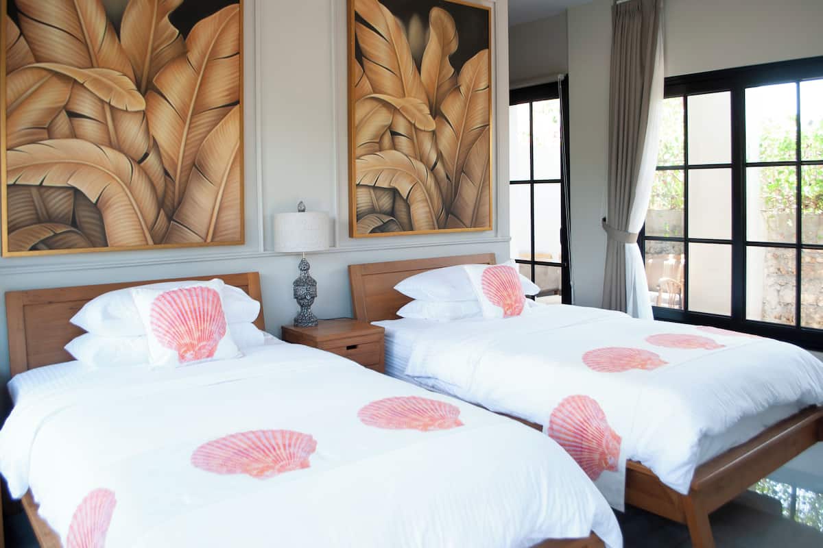 Ett hotellrum med två sängar, stora fönster och en tavla med tropiskt motiv på väggen.