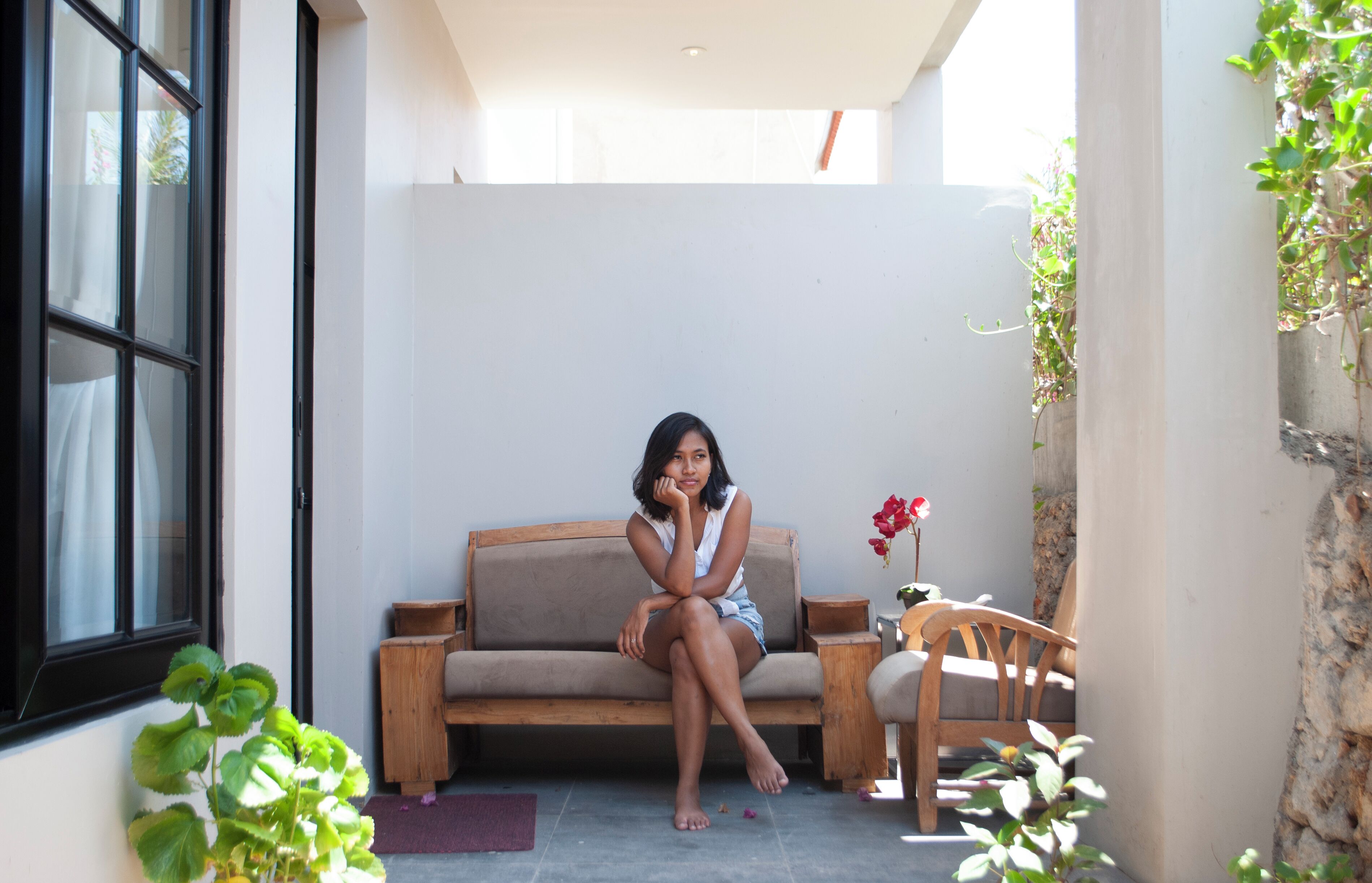 A person sitting on a sofa in a room with a window, a small table, and a chair.