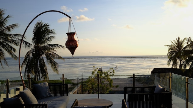 Een balkon met een bank, een tafel en een hangpot, met uitzicht op de oceaan.