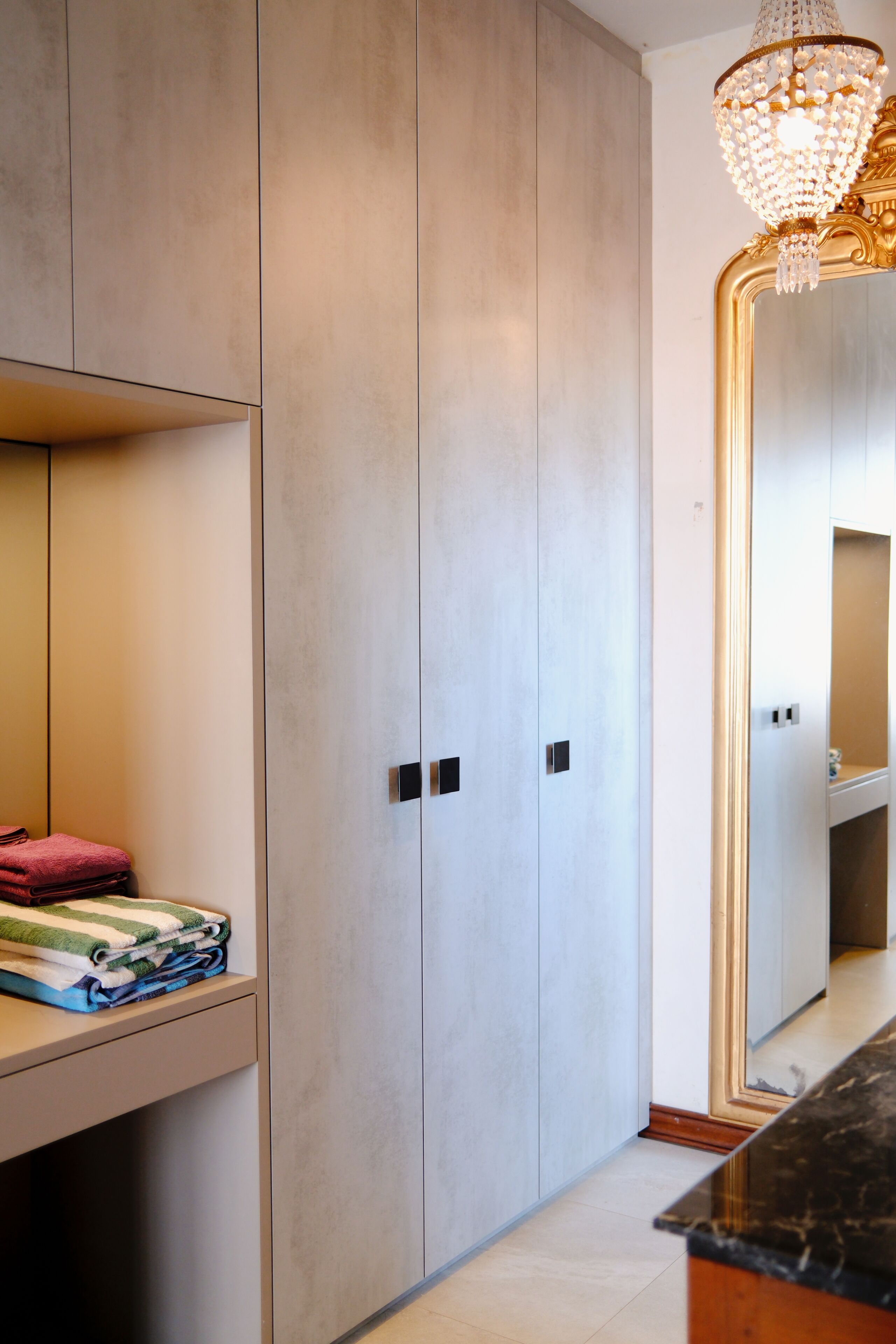 A modern bathroom with a large mirror, a chandelier, and a built-in vanity with a countertop.