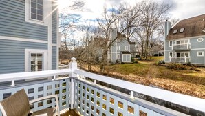 A wooden deck with a white railing, a chair, and a view of a residential area with houses and a river.