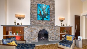 A living room with a stone fireplace, two sofas with patterned cushions, and a large abstract painting above the fireplace.