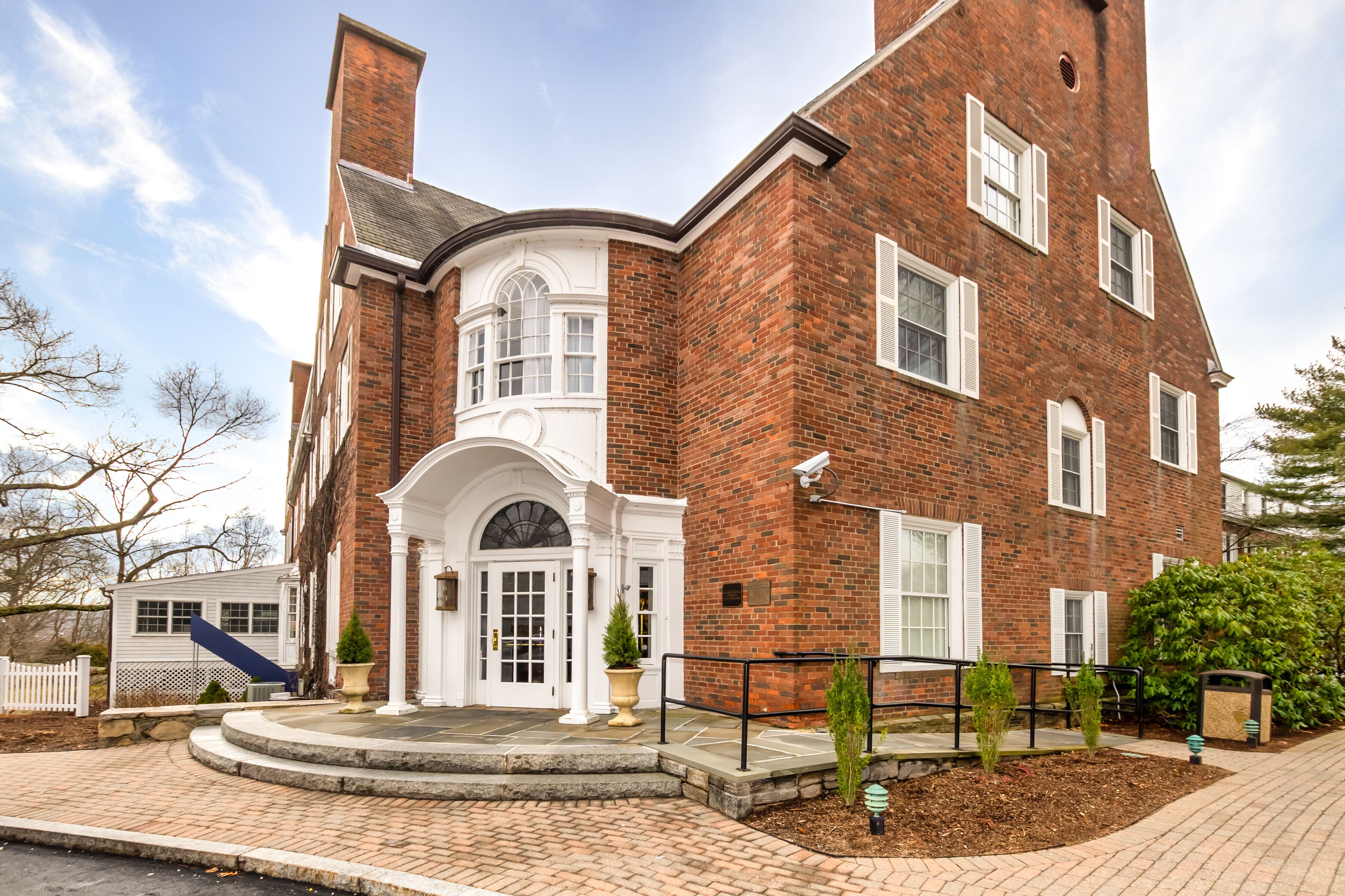 A brick building with a white entrance, a small porch, and a brick pathway leading to the entrance.