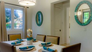 Uma sala de jantar com uma mesa posta para quatro pessoas, uma peça central decorativa e dois espelhos na parede.