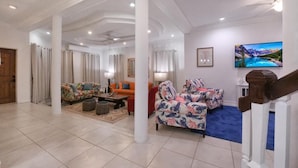 Uma sala de estar ampla com carpete azul, escada de madeira e uma televisão grande na parede.