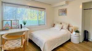 Un dormitorio con cama, escritorio y silla. Se observa una ventana con persianas, una lámpara en el techo y una decoración en la pared.