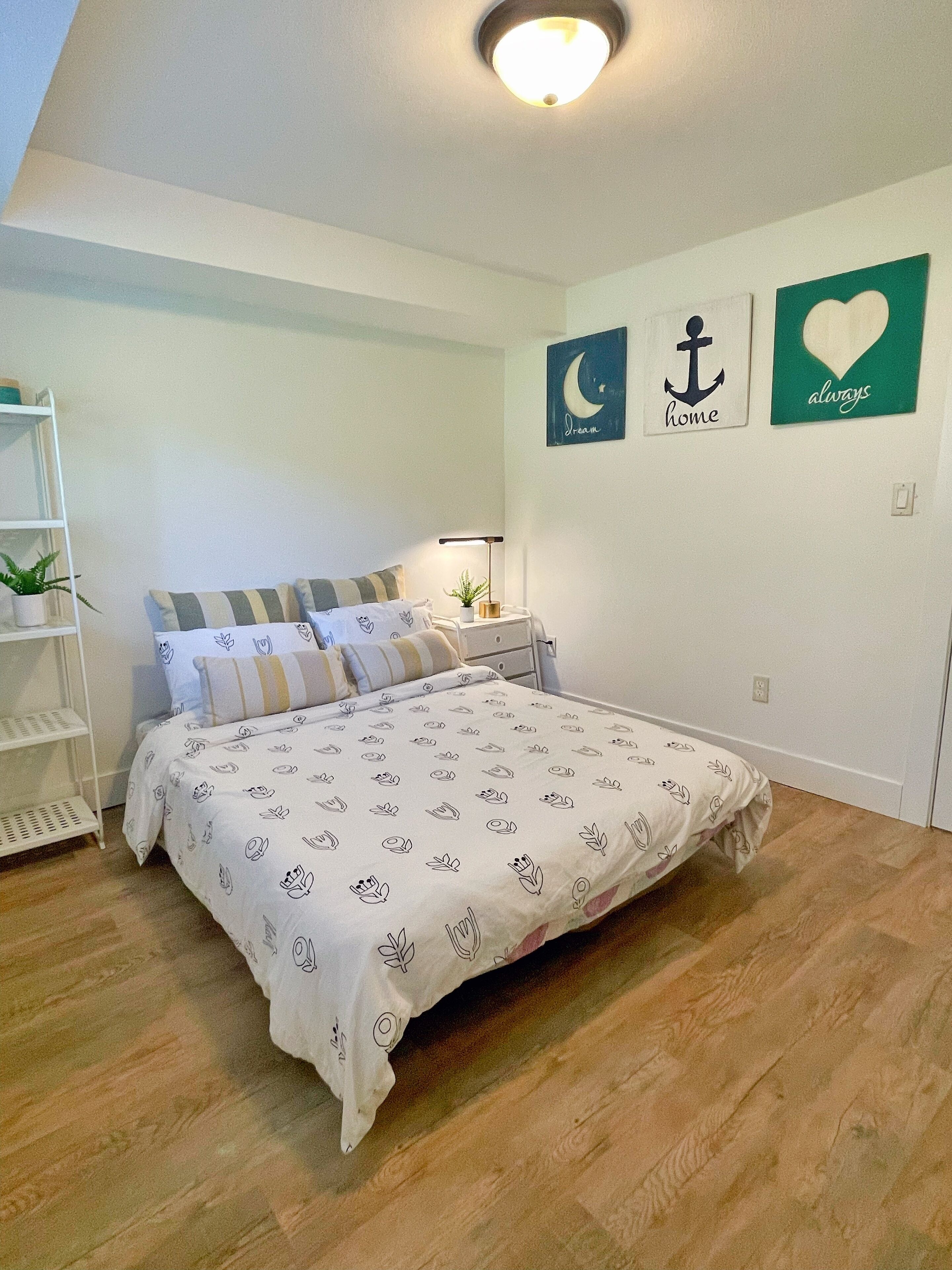 Ein Schlafzimmer mit einem Bett, einem Nachttisch, einem Regal mit Pflanzen und Wanddekorationen, darunter ein Mond, ein Anker und ein Herz.