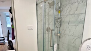 Un baño moderno con ducha envuelta en vidrio, inodoro blanco y pared revestida de mármol.