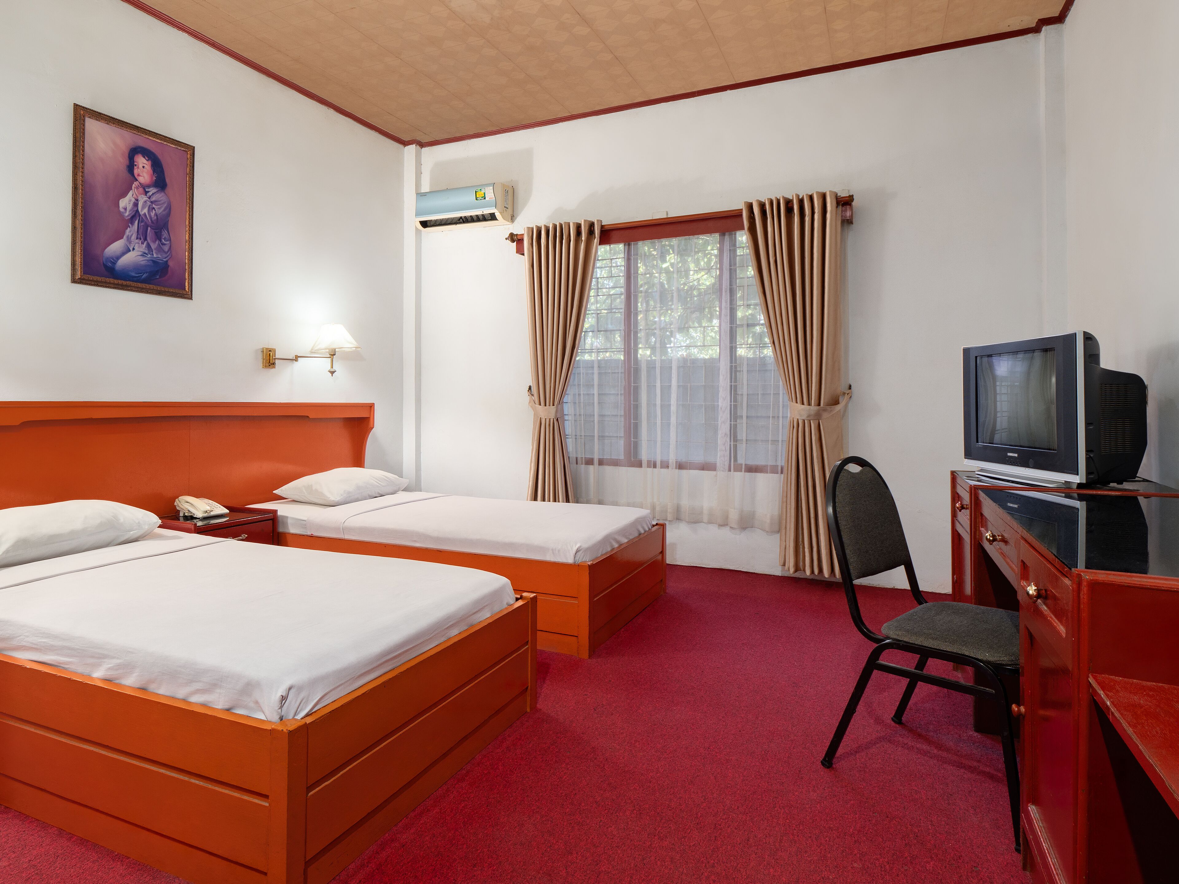 Habitación de hotel con dos camas, un escritorio con televisor, una silla, una ventana con cortinas y un equipo de aire acondicionado.