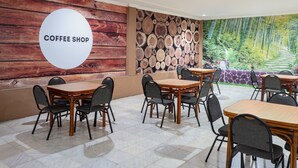 A coffee shop with wooden tables and chairs, a wall with a 'Coffee Shop' sign, and a mural of a forest.