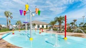 Ein Wasserpark mit Pool, bunten Wasserspielen, Palmen und einem Gebäude im Hintergrund.