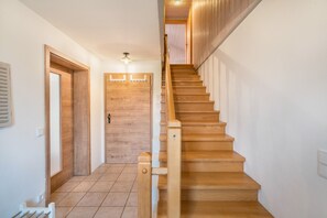 Eine Holztreppe mit Handlauf, eine Tür mit Lichtschalter und eine Deckenleuchte.
