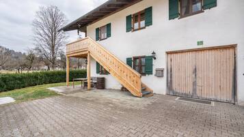 A building with a wooden staircase leading to a balcony, a large garage door, and a paved courtyard.