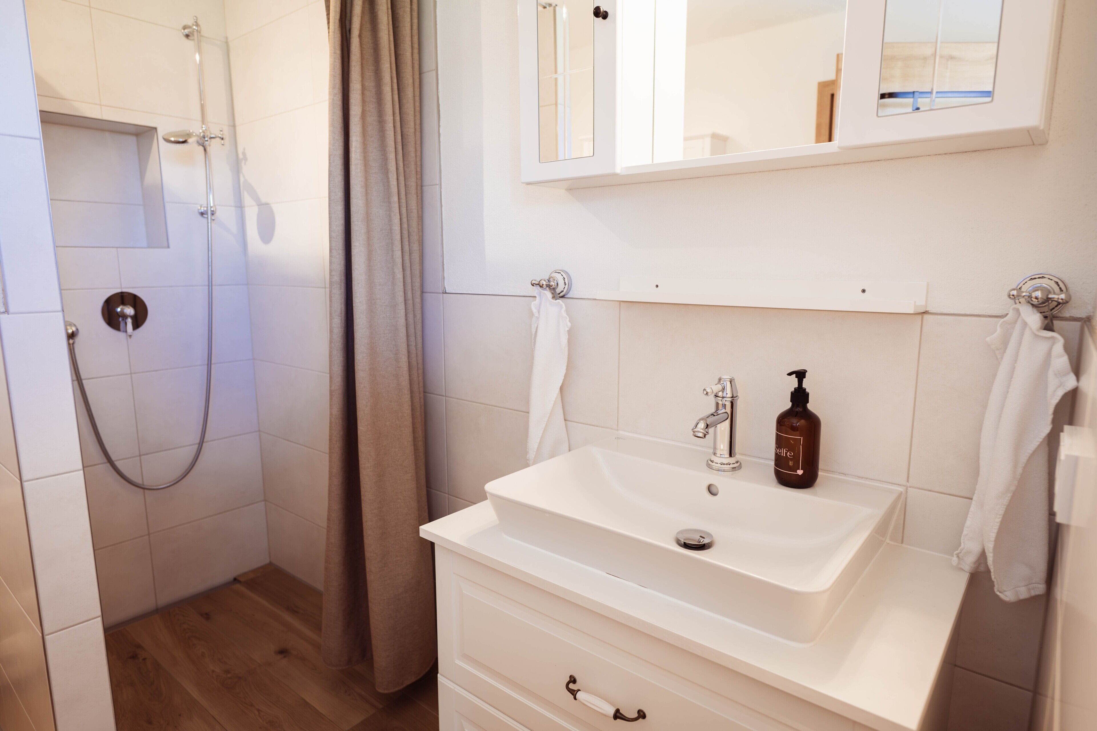 Une salle de bain avec une douche, un lavabo muni d’un distributeur de savon et un miroir au-dessus du lavabo.