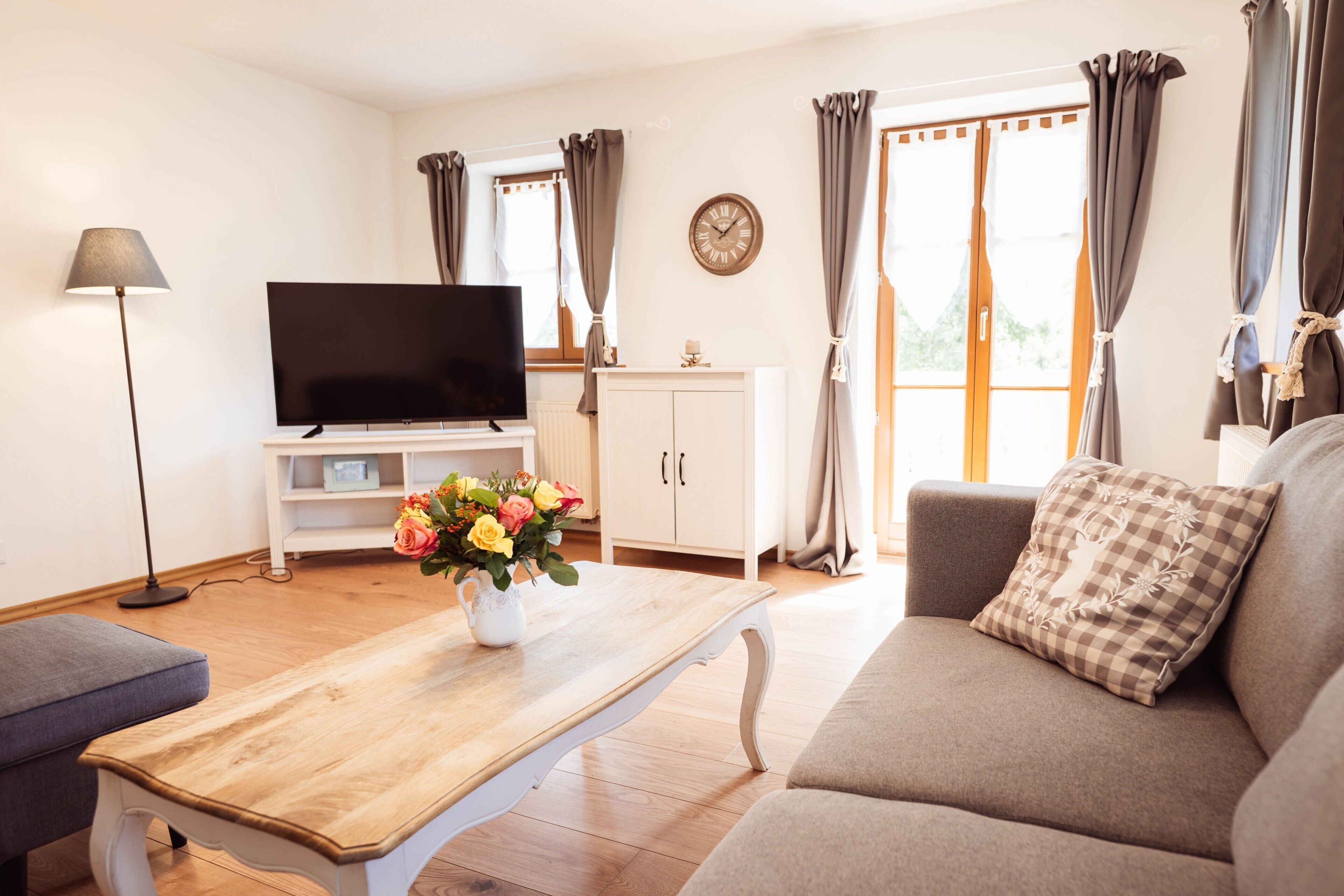 Ein Wohnzimmer mit Flachbildfernseher, einem Couchtisch mit Blumenvase, einer Couch mit kariertem Kissen und einer Lampe.