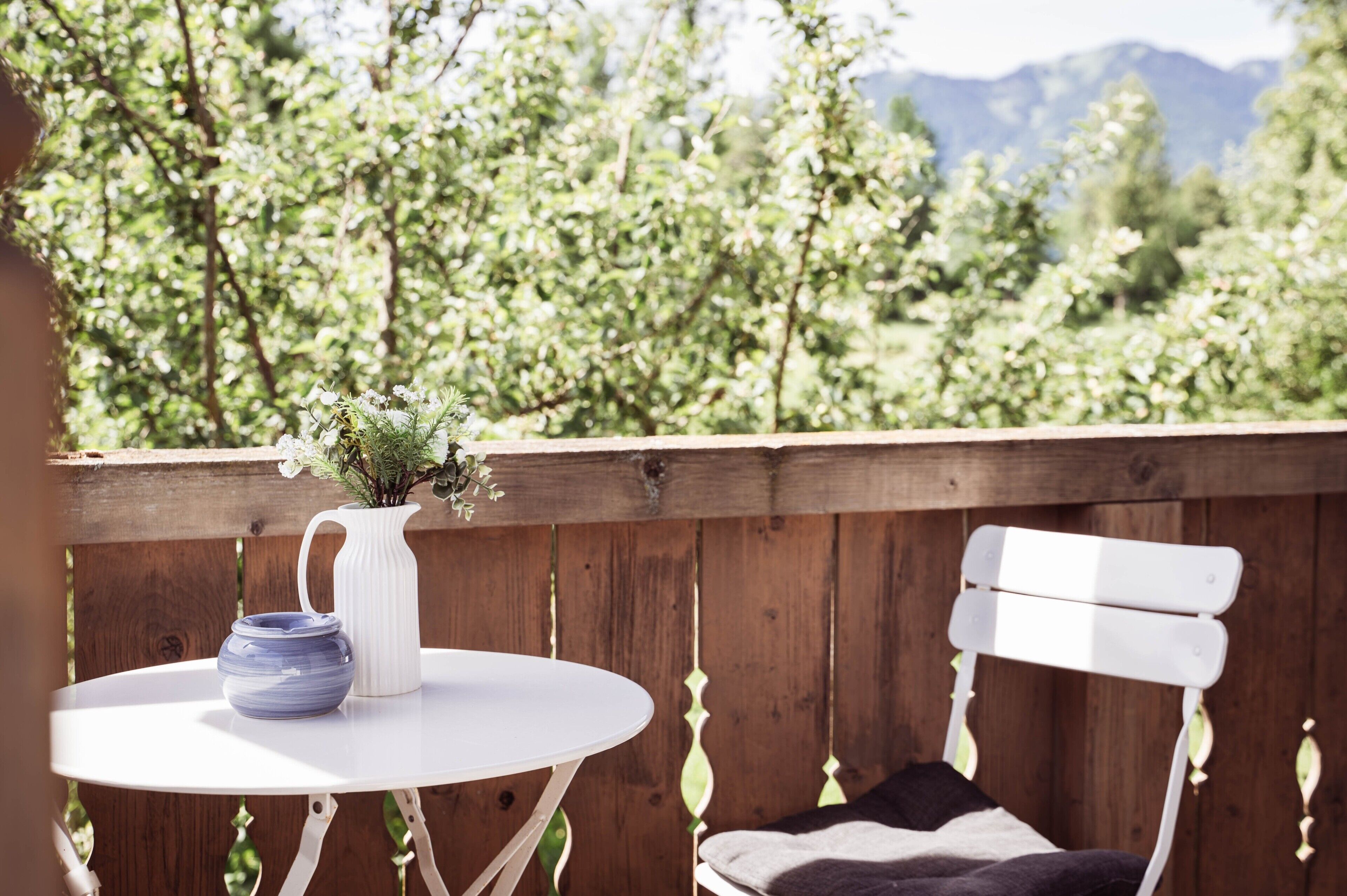 Eine Holzterrasse mit einem weißen Tisch und einer Bank, einer weißen Vase mit Blumen und einer blauen Schüssel.