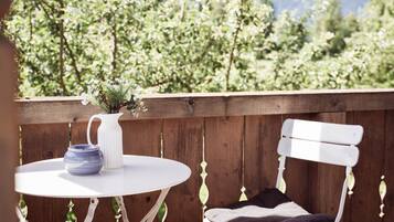 Eine Holzterrasse mit einem weißen Tisch und einer Bank, einer weißen Vase mit Blumen und einer blauen Schüssel.