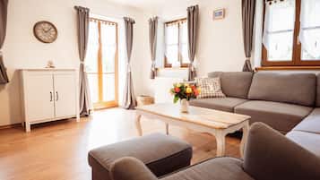 A living room with a sofa, a coffee table with a vase of flowers, a cabinet, and curtains on the windows.