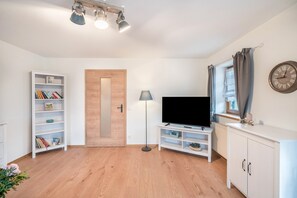Ein Wohnzimmer mit Bücherregal, Fernseher, Lampe, einer Uhr und einer Holztür.