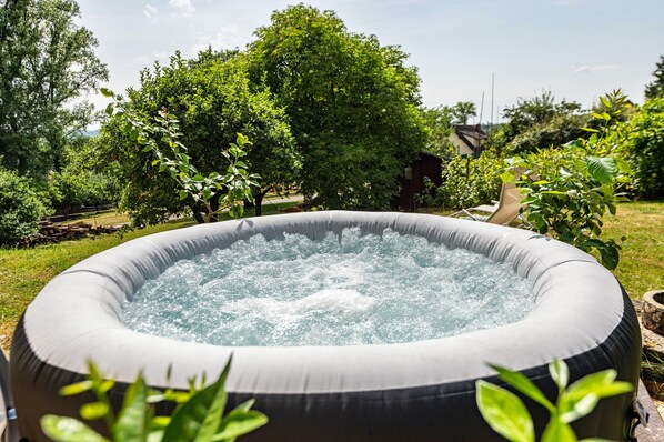 An inflatable hot tub in a garden with trees and a shed in the background.