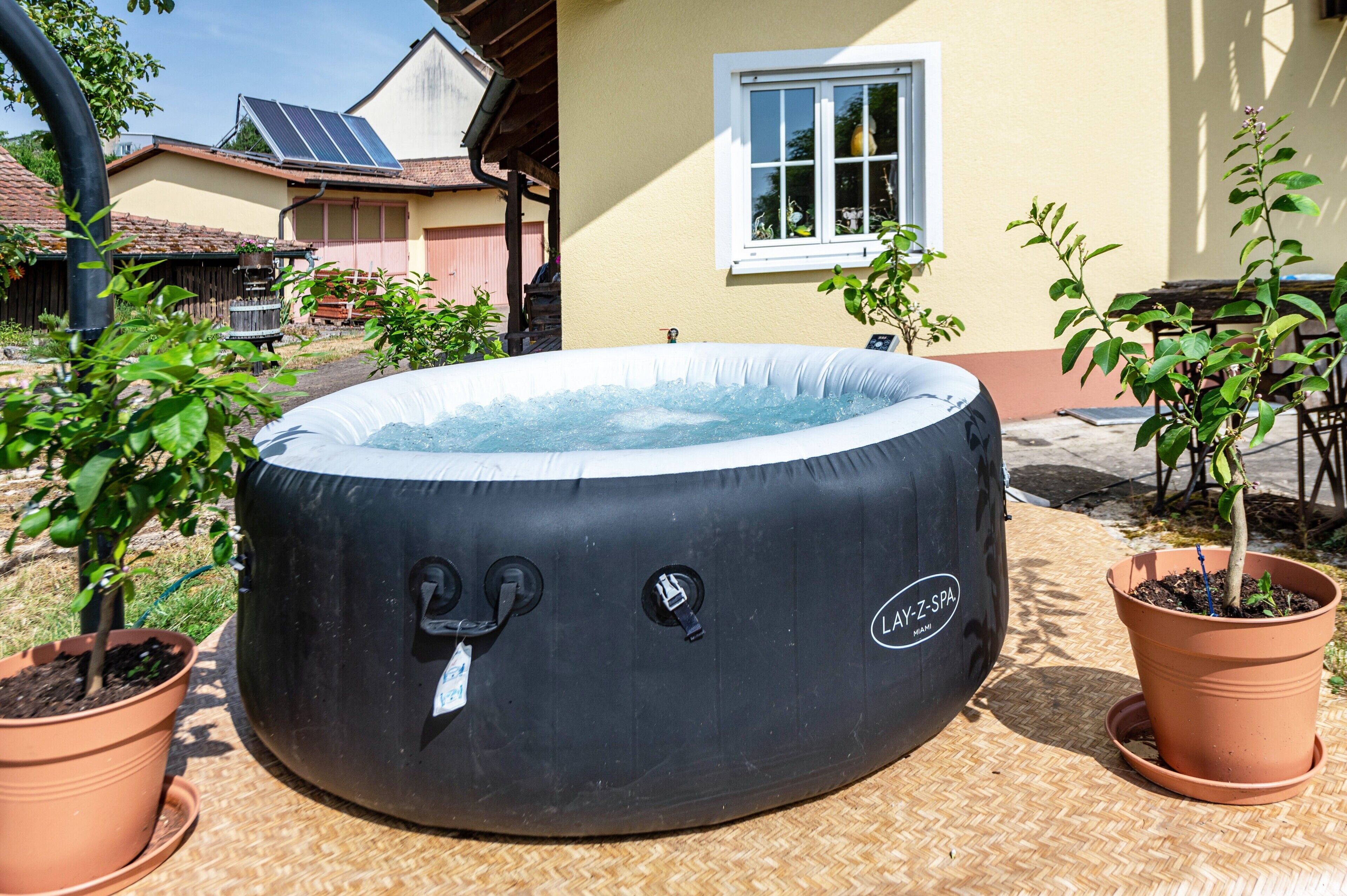 Een hottub in een tuin met potplanten, een raam en een huis op de achtergrond.