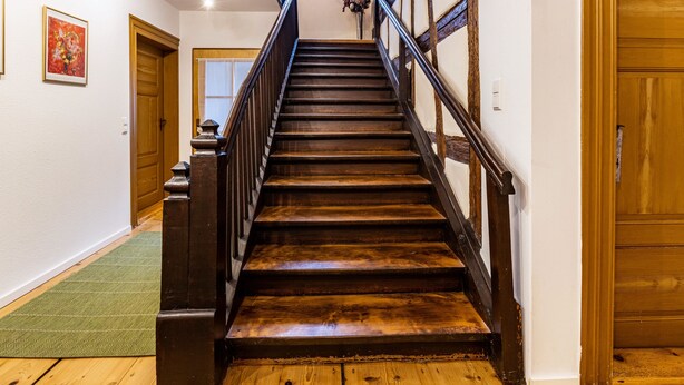 Una escalera de madera con barandilla, un tapete verde en la parte inferior y una puerta arriba.