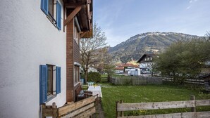 Una casa con facciata in legno, un tavolo con sedie all'esterno e una montagna sullo sfondo.